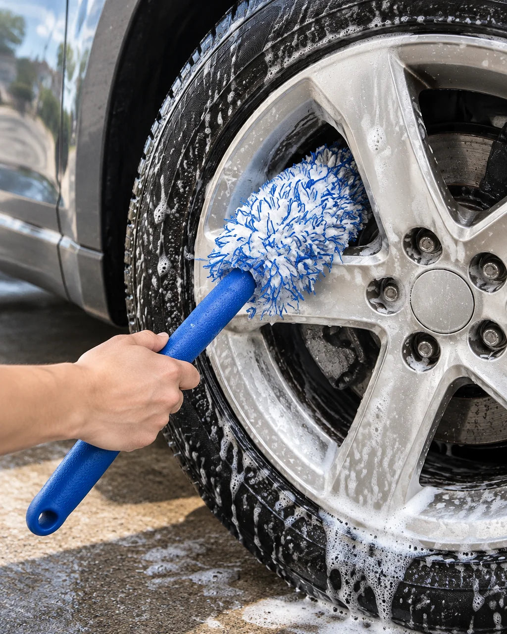 Show this exact soft wheel and rim detailing brush being used on a real vehicle wheel, with the plus