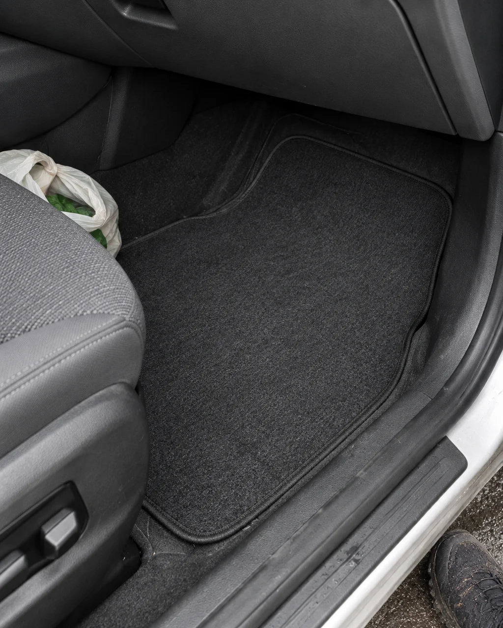 A photograph of the exact dark carpet universal car floor mat from the reference installed in the fr