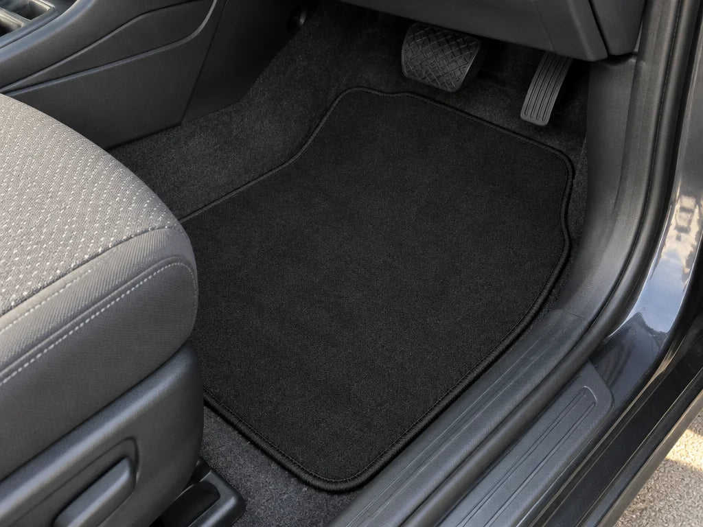 Show a close detail of these exact carpet floor mats in a vehicle footwell, including the edge and s