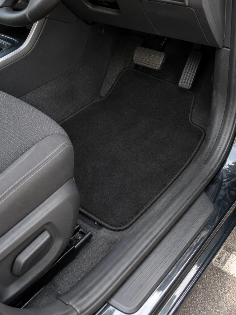 Show these exact universal carpet car floor mats installed in the front footwell of a real vehicle.