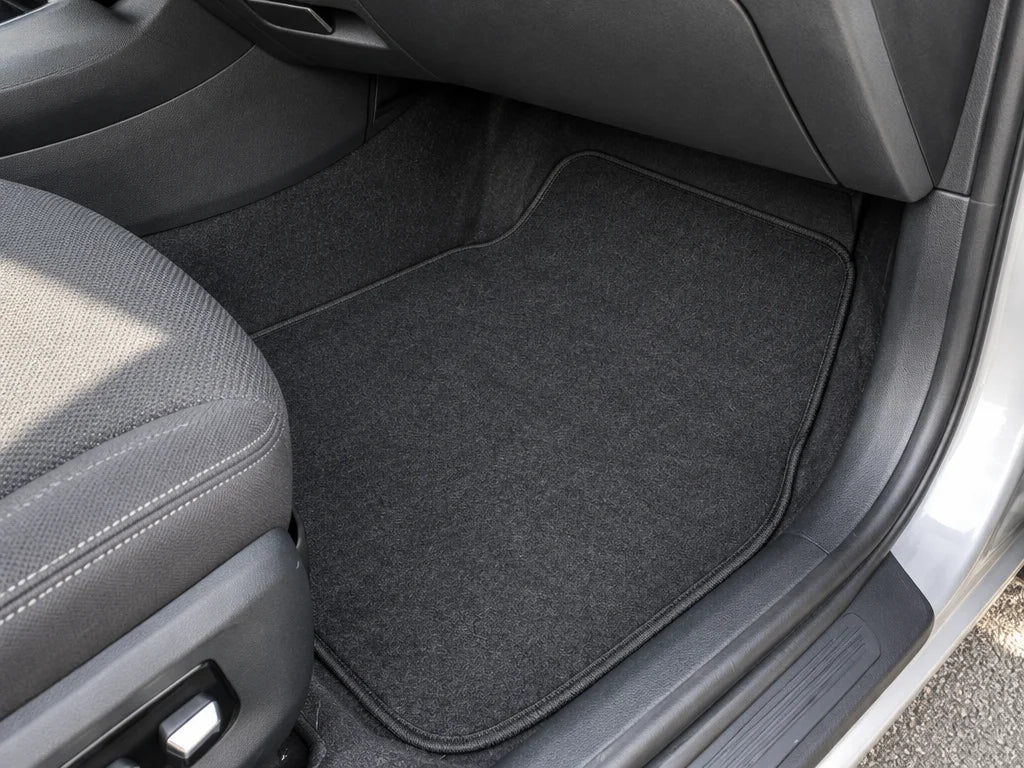 Show a close detail of these exact carpet floor mats lying in a vehicle footwell, including the edge