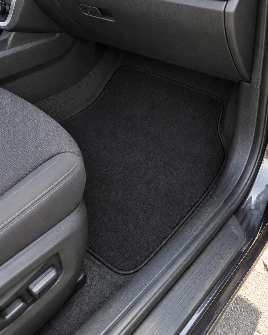 Show these exact universal carpet car floor mats installed in the front footwell of a real vehicle,